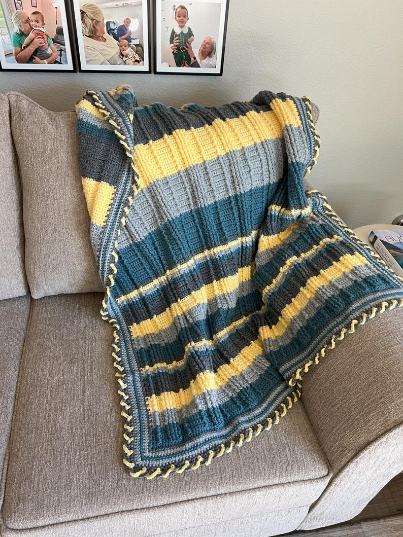May include: A striped crocheted throw blanket in shades of teal, gray, and yellow with a yellow crocheted border.