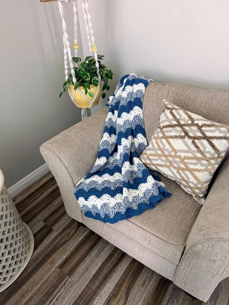 May include: A blue and white crocheted throw blanket with a wave pattern is draped over a light brown armchair. A brown and white patterned pillow is on the chair.