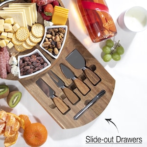 May include: A wooden cheese board with a variety of cheeses, crackers, nuts, and fruit. Includes a set of cheese knives with wooden handles. A bottle of champagne and a small cup are also present. The text "Slide-out Drawers" is visible.