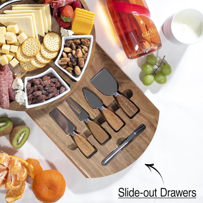 May include: A wooden cheese board with a variety of cheeses, crackers, nuts, and fruit. Includes a set of cheese knives with wooden handles. A bottle of champagne and a small cup are also present. The text "Slide-out Drawers" is visible.