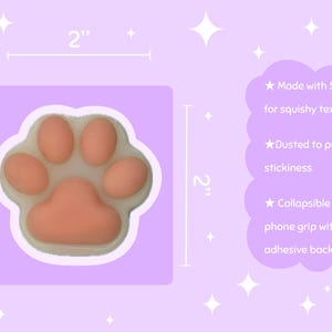 May include: A peach-colored paw-shaped phone grip, 2 inches in size, with a white border, on a lavender background. The grip is made of silicone for a squishy texture and has a collapsible bracket with adhesive backing. Text on the image says it is dusted to prevent stickiness.