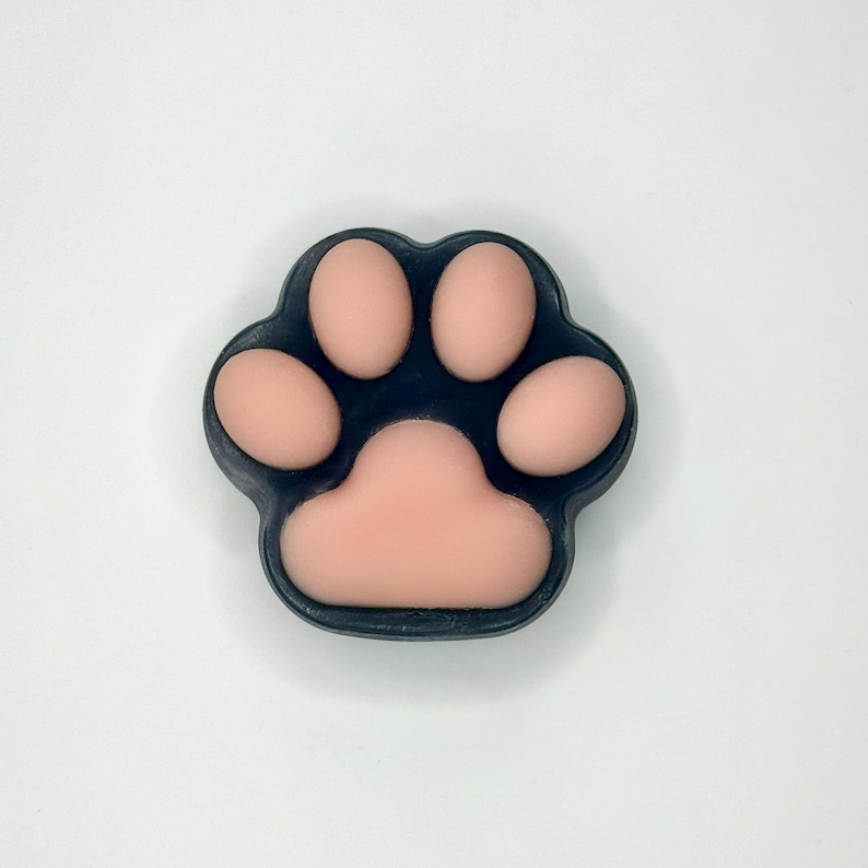 May include: A paw-shaped soap with a dark blue border and light pink pads. The soap is a close-up shot against a white background. The paw print design is a common theme for pet-related products.
