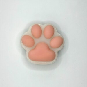 May include: A close-up of a paw-shaped soap with a light pink paw print design. The paw print is surrounded by a white border. The soap is on a white background.