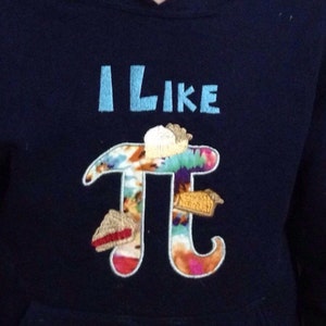 May include: A navy blue hoodie with the text "I like Pi" embroidered in light blue. The Pi symbol is decorated with colourful fabric and pie-shaped embellishments.