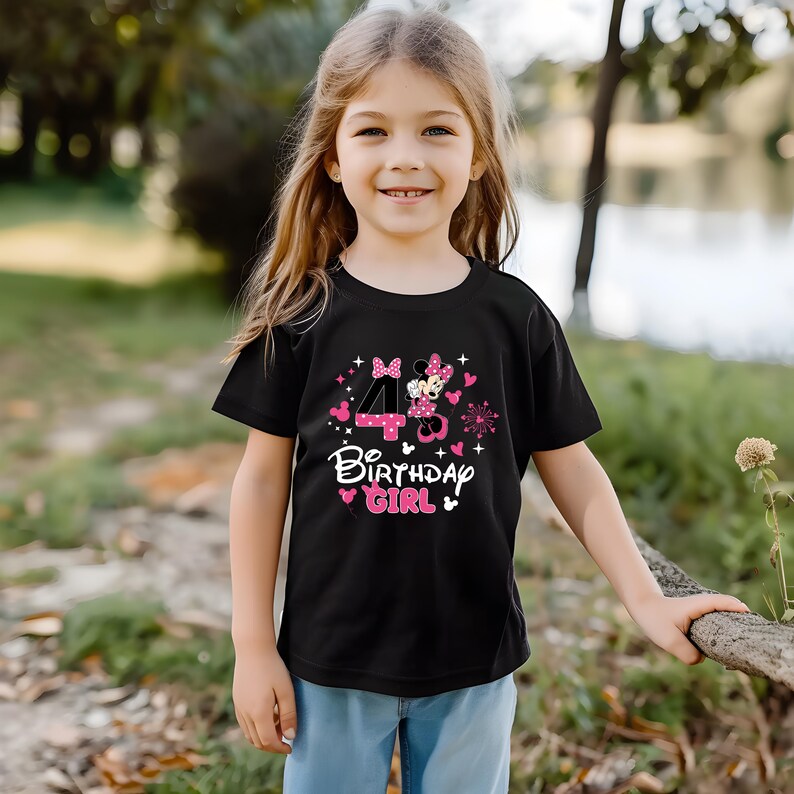 K&ouml;nnte beinhalten: Schwarzes T-Shirt mit Minnie Mouse-Design, der Zahl 4 und dem Schriftzug "Birthday Girl" in Rosa und Wei&szlig;. Das Shirt wird von einem jungen M&auml;dchen mit blonden Haaren getragen, das drau&szlig;en l&auml;chelt.