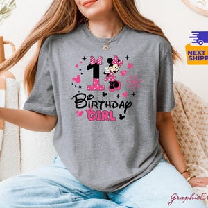 K&ouml;nnte beinhalten: Graues T-Shirt mit einem Minnie-Mouse-Design, der Zahl 1, Herzen und dem Text "Birthday Girl" in Schwarz und Pink. Das Shirt hat einen Rundhalsausschnitt und kurze &Auml;rmel. Das Design beinhaltet eine Minnie-Mouse-Grafik.