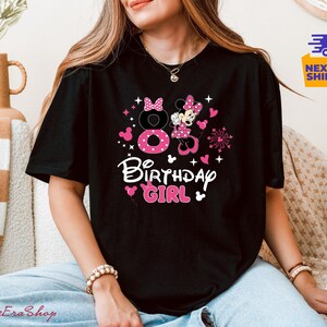 K&ouml;nnte beinhalten: Schwarzes T-Shirt mit einem rosa und wei&szlig;en Minnie-Maus-Design. Das Design umfasst die Zahl 8, Herzen, Sterne und die Worte "Birthday Girl". Das Shirt ist ein l&auml;ssiger Stil.
