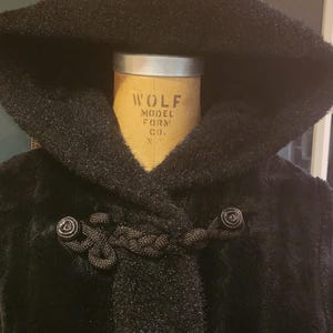 Peut inclure: Manteau noir à capuche avec fermeture à corde et bouton. Le manteau est fait d'un tissu doux et duveteux. L'étiquette sur le mannequin indique "Wolf Model Form Co."