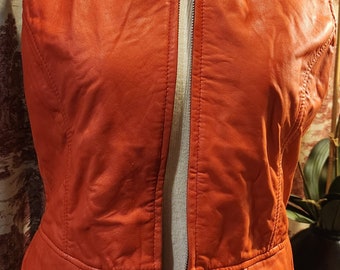 May include: A sleeveless, burnt orange leather vest with a zipper closure. The vest has a collar and a fitted waist.
