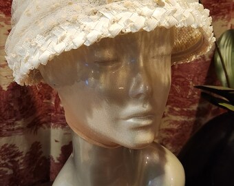 Puede incluir: Un sombrero de encaje blanco con una cinta blanca y un borde de encaje blanco. El sombrero está en una cabeza de maniquí blanca.