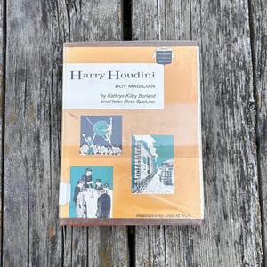 May include: A hardcover book titled Harry Houdini Boy Magician by Kathryn Kilby Borland and Helen Ross Speicher, illustrated by Fred M. Irvin. The cover features a tan background with two black and white illustrations depicting a magician and a train.