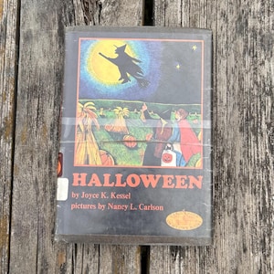 Może przedstawiać: Książka w twardej oprawie zatytułowana Halloween autorstwa Joyce K. Kessel z ilustracjami Nancy L. Carlson. Okładka przedstawia czarną sylwetkę czarownicy lecącej na tle ż&oacute;łtego księżyca nad polem dyń z dwiema postaciami w kostiumach.