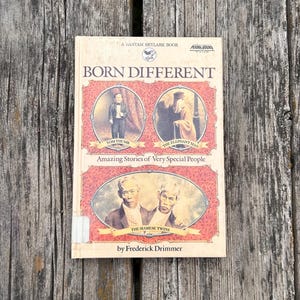 Pu&ograve; includere: Un libro tascabile intitolato Born Different di Frederick Drimmer. La copertina presenta tre ritratti ovali di personaggi storici etichettati come Tom Thumb, The Elephant Man e The Siamese Twins, su uno sfondo rosso a motivi.