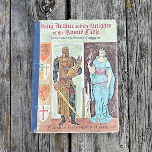 Może przedstawiać: Książka w twardej oprawie zatytułowana King Arthur and the Knights of the Round Table, z ilustracjami Gustafa Tenggrena. Okładka przedstawia rycerza w zbroi i kobietę w niebieskiej sukni, z herbami oraz napisem A Golden Illustrated Classic.
