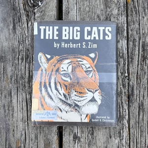 Puede incluir: Un libro de tapa dura titulado The Big Cats de Herbert S. Zim, ilustrado por Gardell D. Christensen. La sobrecubierta negra presenta una ilustraci&oacute;n detallada de un tigre naranja y negro, una pegatina de Morrow Eagle Library Edition y texto blanco.