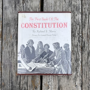 Puede incluir: Un libro de tapa dura titulado The First Book of The Constitution de Richard B. Morris con ilustraciones de Leonard Everett Fisher. La cubierta blanca presenta una ilustraci&oacute;n en blanco y negro de figuras hist&oacute;ricas firmando un documento.