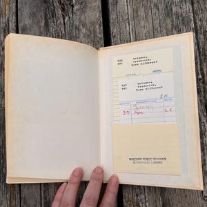 Pu&ograve; includere: Un libro con copertina rigida aperto con una pagina color crema e una tasca per la scheda della biblioteca. La scheda mostra il testo Brimmer, Frederick, Born different, Wallowa Public Schools Elementary Library e nomi scritti a mano.