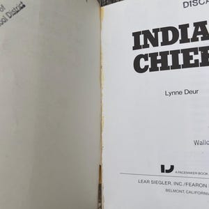 Może przedstawiać: Otwarte strony książki zatytułowanej Indian Chiefs autorstwa Lynne Deur, wydanej przez Lear Siegler, Inc./Fearon w Belmont w Kalifornii. Na lewej stronie widoczny jest odręczny tekst i pieczątka, a na prawej tytuł oraz informacje o wydawcy.
