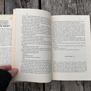 K&ouml;nnte beinhalten: Ein aufgeschlagenes Taschenbuch mit dem Titel Roots von Alex Haley, das gedruckten Text auf cremefarbenen Seiten zeigt. Die linke Seite enth&auml;lt ein Vorwort, w&auml;hrend die rechte Seite den Beginn von Kapitel 16 zeigt. Das Buch ist aufgeschlagen.