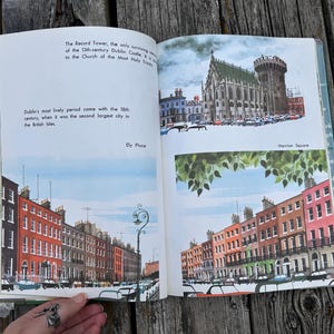 Peut inclure: Un livre ouvert pr&eacute;sentant des illustrations de monuments de Dublin, notamment la Record Tower, le ch&acirc;teau de Dublin, Ely Place et Merrion Square. Les pages contiennent du texte imprim&eacute; d&eacute;crivant l'histoire de la ville avec des peintures architecturales.