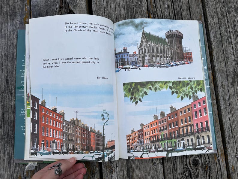 Peut inclure: Un livre ouvert pr&eacute;sentant des illustrations de monuments de Dublin, notamment la Record Tower, le ch&acirc;teau de Dublin, Ely Place et Merrion Square. Les pages contiennent du texte imprim&eacute; d&eacute;crivant l'histoire de la ville avec des peintures architecturales.