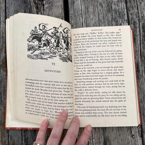 May include: An open vintage book with cream-colored pages featuring black ink text and a black and white illustration of figures on horseback. The chapter heading reads VI ADVENTURE and the page number 41 is visible in the top corner.