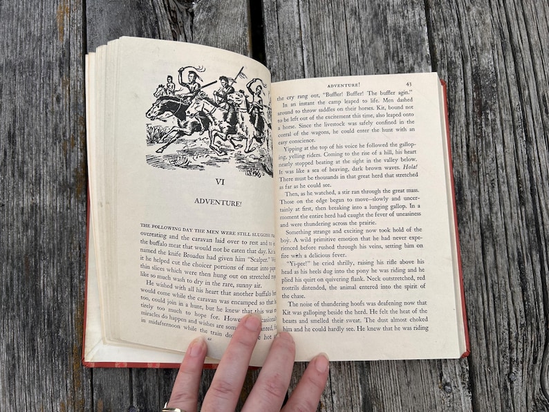 May include: An open vintage book with cream-colored pages featuring black ink text and a black and white illustration of figures on horseback. The chapter heading reads VI ADVENTURE and the page number 41 is visible in the top corner.