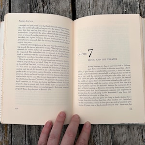 May include: An open book titled Russian Journey with cream-coloured pages and black text. The left page contains paragraphs of text, while the right page displays Chapter 7, Music and the Theater, with page numbers 154 and 155 visible at the bottom.