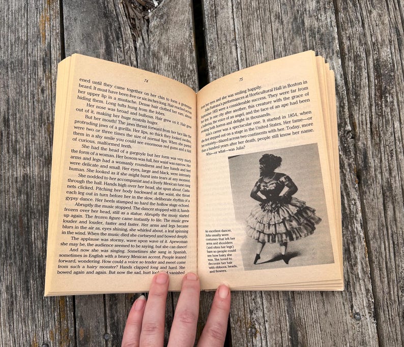 Pu&ograve; includere: Un libro aperto con pagine color beige contenente testo stampato e una fotografia in bianco e nero di una persona con un abito a balze. La pagina sinistra presenta diversi paragrafi, mentre quella destra include testo e l'immagine di un artista.