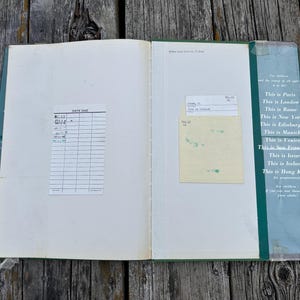Peut inclure: Un livre de biblioth&egrave;que vintage ouvert avec une fiche de pr&ecirc;t blanche sur la page de gauche et une pochette jaune avec une carte sur la page de droite. La couverture int&eacute;rieure vert fonc&eacute; liste des villes comme Paris, Londres et Rome en blanc.