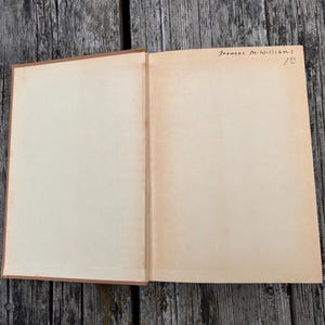 K&ouml;nnte beinhalten: Ein aufgeschlagenes Hardcover-Buch mit leeren, cremefarbenen Seiten. In der oberen rechten Ecke der rechten Seite befindet sich handschriftlicher Text in schwarzer Tinte, der Frances M. Williams und die Zahl 122 lautet. Brauner Buchr&uuml;cken.