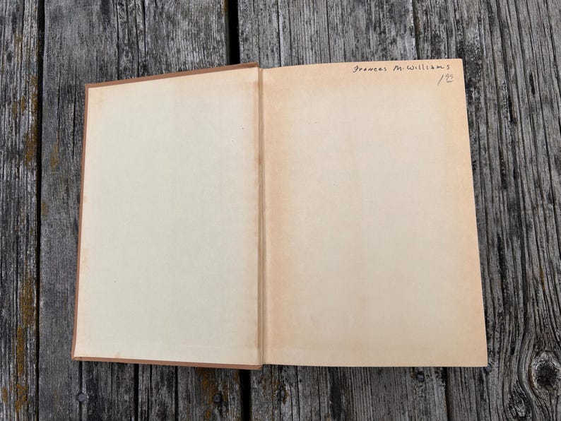K&ouml;nnte beinhalten: Ein aufgeschlagenes Hardcover-Buch mit leeren, cremefarbenen Seiten. In der oberen rechten Ecke der rechten Seite befindet sich handschriftlicher Text in schwarzer Tinte, der Frances M. Williams und die Zahl 122 lautet. Brauner Buchr&uuml;cken.