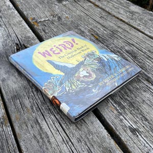 以下が含まれることがあります： ピーター・R・リンバーグ著、ベッツィー・リューイン絵のハードカバー本『Weird! The Complete Book of Halloween Words』。表紙には大きな黄色い月と、とんがり帽子をかぶった魔女のカラフルなイラストが描かれています。