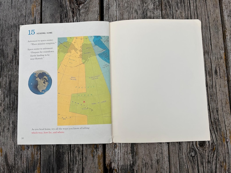 May include: An open book page titled 15 Heading Home, featuring a dialogue between an astronaut and space centre, a small circular image of Earth, and a colourful map showing time zones and the Pacific Ocean with a red X marking Hawaii.