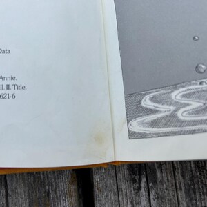 May include: A book page featuring black text on the left side including Publication Data, 9-1916, Little Orphan Annie, and ISBN 0-397-31621-6. The right side displays a black and white illustration of bubbles rising from a wavy, textured surface.