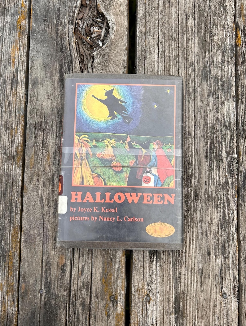 Może przedstawiać: Książka w twardej oprawie zatytułowana Halloween autorstwa Joyce K. Kessel z ilustracjami Nancy L. Carlson. Okładka przedstawia czarną sylwetkę czarownicy lecącej na tle ż&oacute;łtego księżyca nad polem dyń z dwiema postaciami w kostiumach.