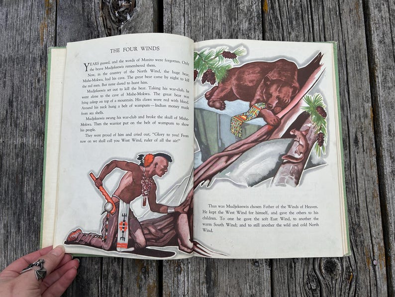 K&ouml;nnte beinhalten: Ein aufgeschlagenes Vintage-M&auml;rchenbuch mit dem Titel The Four Winds mit gedrucktem Text und farbigen Illustrationen. Die linke Seite zeigt einen Krieger mit einer Keule, w&auml;hrend die rechte Seite einen Braunb&auml;ren auf einem Ast darstellt.