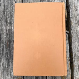 K&ouml;nnte beinhalten: Ein rechteckiges Hardcover-Buch mit einem einfarbigen, hellbraunen oder beigen Stoffeinband. Das Buch ist vertikal ausgerichtet und zeigt den Vorderdeckel sowie die Buchr&uuml;cken-Kante auf der rechten Seite mit einer schlichten Oberfl&auml;che.