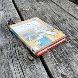 May include: A hardback book titled Clyde Beatty Boy Animal Trainer by Katherine Wilkie. The cover features a tan background with a blue spine and a graphic illustration of a person training animals. The book has a bright red edge on the pages.