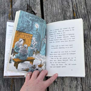 Puede incluir: Un libro de tapa dura abierto que presenta una ilustraci&oacute;n en color de tres mujeres sentadas junto a una chimenea en la p&aacute;gina izquierda y texto impreso en la derecha. El texto incluye las l&iacute;neas: When shall we three meet again, In thunder, lightning, or in rain?