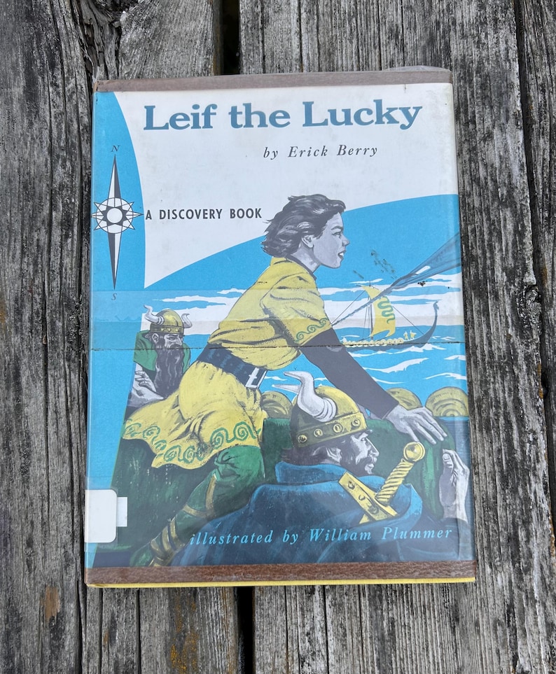 Pu&ograve; includere: Un libro con copertina rigida intitolato Leif the Lucky di Erick Berry, illustrato da William Plummer. La copertina presenta un'illustrazione blu, gialla e verde di figure in abiti vichinghi su una nave, con una rosa dei venti e il testo A Discovery Book.