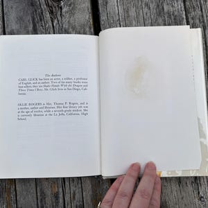 May include: An open hardcover book with white pages. The left page features text under the heading The Authors, detailing biographies for Carl Glick and Ollie Rogers. The right page is blank with a faint, circular yellowish stain near the center.