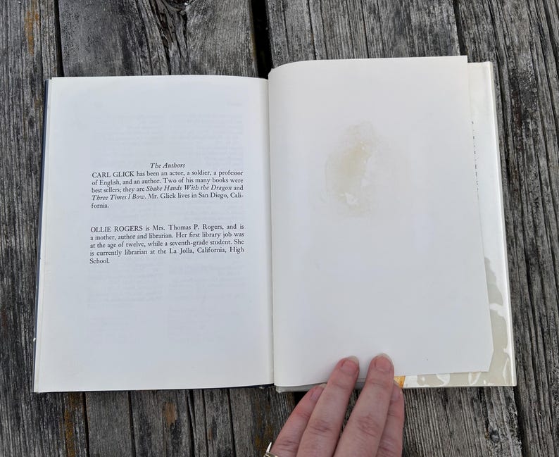 May include: An open hardcover book with white pages. The left page features text under the heading The Authors, detailing biographies for Carl Glick and Ollie Rogers. The right page is blank with a faint, circular yellowish stain near the center.