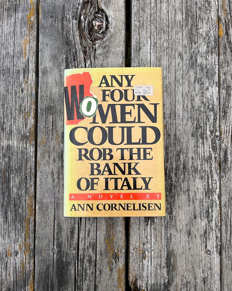 May include: A paperback book titled Any Four Women Could Rob The Bank Of Italy, a novel by Ann Cornelisen. The cover is yellow with bold black text, a red graphic element behind the word Women, and a small green circular sticker on the front.