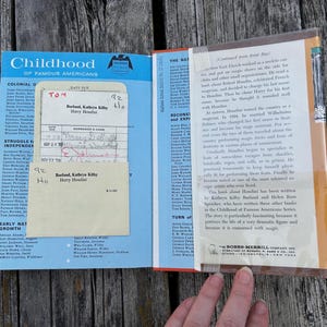 May include: A vintage hardcover book from the Childhood of Famous Americans series titled Harry Houdini by Kathryn Kilby Borland and Helen Ross Speicher. The inside cover features a blue library checkout card pocket with a paper date due slip.