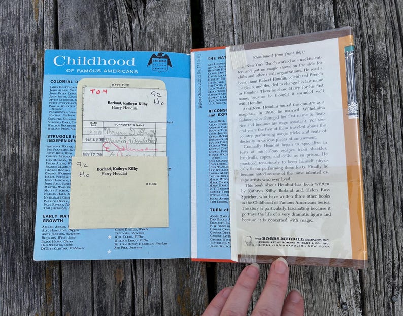 May include: A vintage hardcover book from the Childhood of Famous Americans series titled Harry Houdini by Kathryn Kilby Borland and Helen Ross Speicher. The inside cover features a blue library checkout card pocket with a paper date due slip.