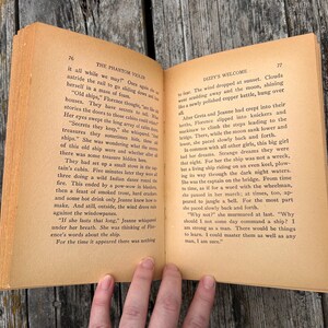 K&ouml;nnte beinhalten: Ein aufgeschlagenes altes Buch mit gealterten, vergilbten Seiten und schwarzem Drucktext. Die linke Seite tr&auml;gt den Titel The Phantom Violin, Seite 76, und die rechte Seite den Titel Dizzy's Welcome, Seite 77. Das Buch zeigt zwei Textspalten.