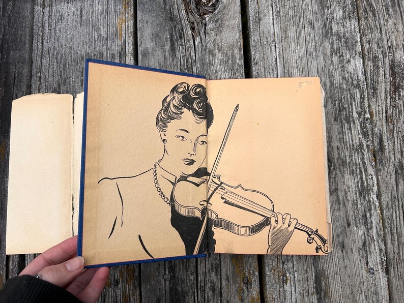 May include: A vintage book with a tan endpaper illustration featuring a black ink line drawing of a person with an updo hairstyle wearing a necklace and playing a violin with a bow. The book has a dark blue spine and aged paper edges.