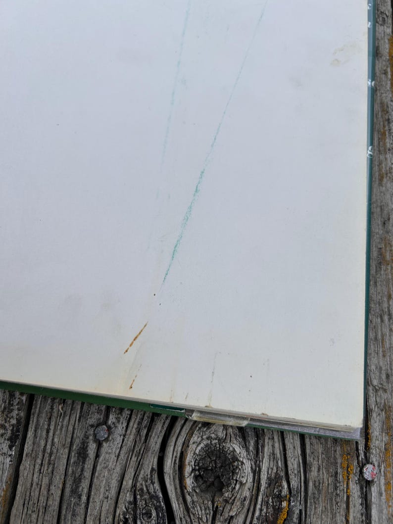 Peut inclure: Un livre &agrave; couverture vert fonc&eacute; avec des pages blanc cass&eacute;. La page ouverte pr&eacute;sente une fine ligne diagonale bleu sarcelle trac&eacute;e &agrave; l'encre ou au crayon, ainsi qu'une petite tache brun clair pr&egrave;s du coin inf&eacute;rieur gauche de la page.