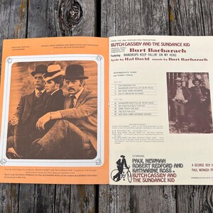 K&ouml;nnte beinhalten: Ein Vintage-Notenbuch f&uuml;r Klavier und Gesang zum Film Butch Cassidy und Sundance Kid. Das Cover zeigt ein sepiafarbenes Foto der Hauptfiguren, eine Titelliste sowie Credits f&uuml;r Burt Bacharach, Hal David, Paul Newman und Robert Redford.